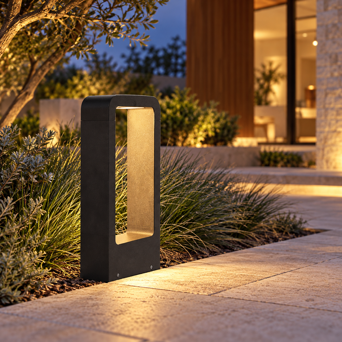 Warm-lit black bollard beside ornamental grasses and a garden path